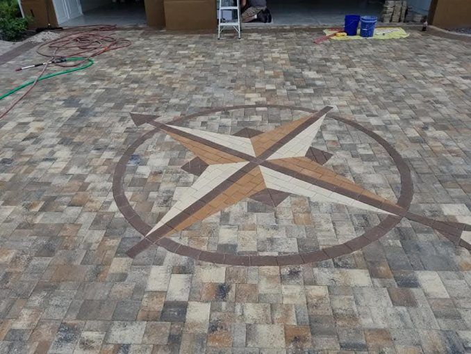 A compass rose inlay of beige and brown pavers centered in a multi-toned stone driveway.