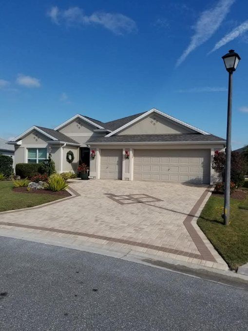 A suburban, single-story house with a beige exterior, a multi-car garage, and a decorative paved driveway under blue sky.