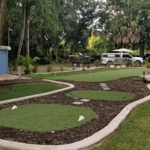 A small backyard putting green with several circular turf areas and golf cups, surrounded by mulch and grass.
