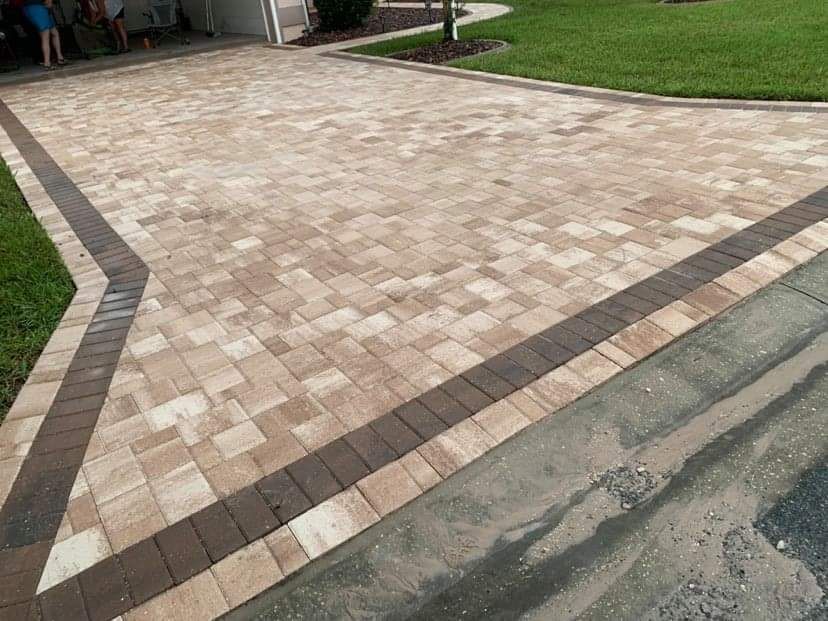 A driveway made of light tan rectangular pavers with a dark brown border leading to a garage.