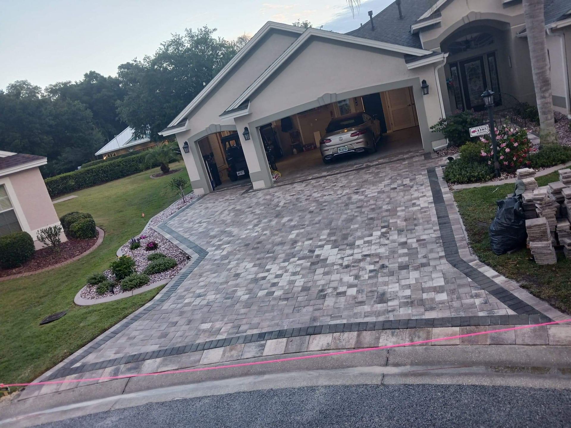 A newly installed paver driveway with a dark border and a curved stone planter in front of a house garage.