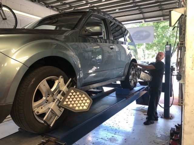 Blue SUV on an alignment lift in a garage, with a technician adjusting the wheel alignment.