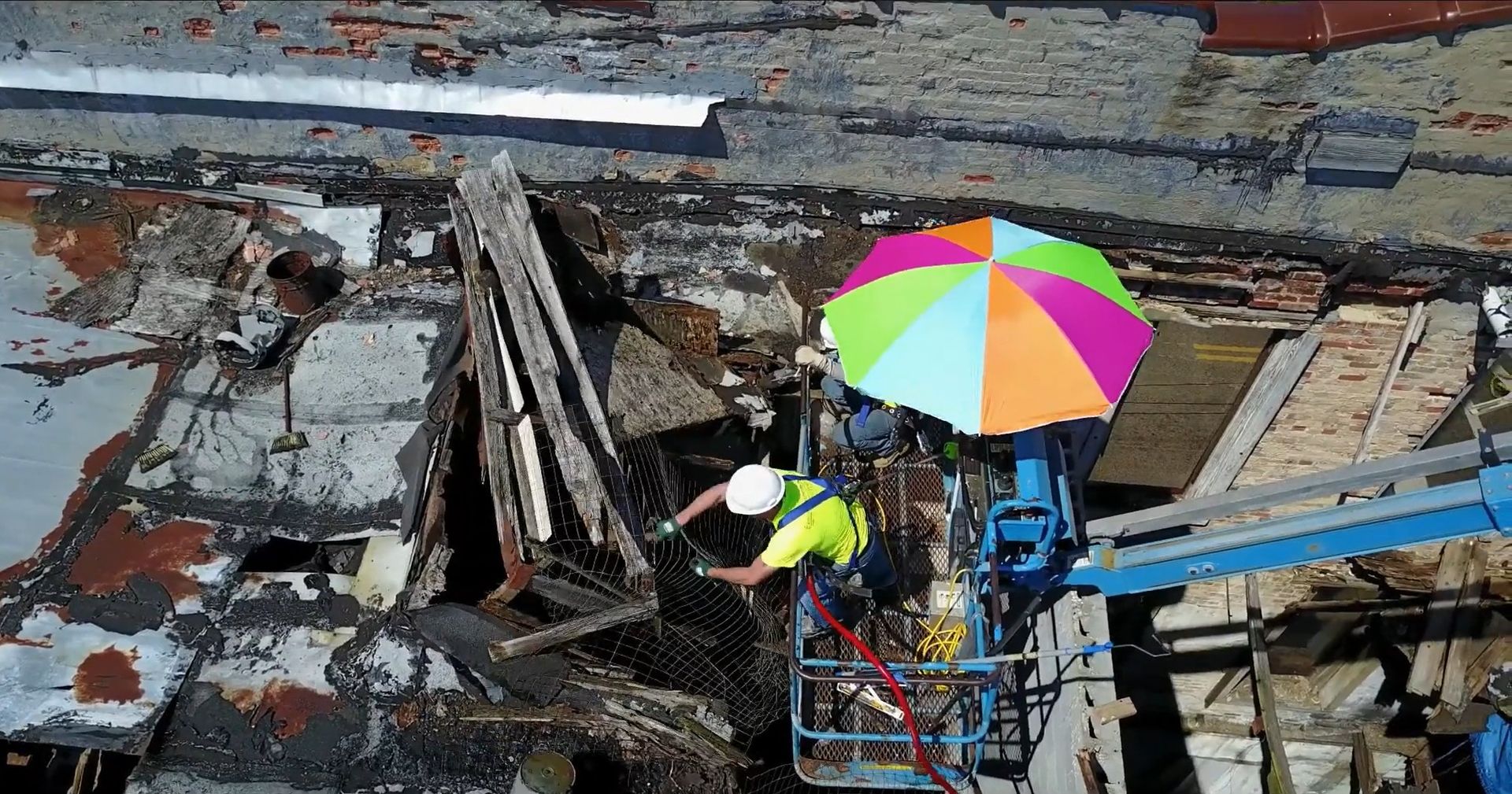 A construction worker repairs a building, protected by a colorful umbrella on a lift in North Carolina.