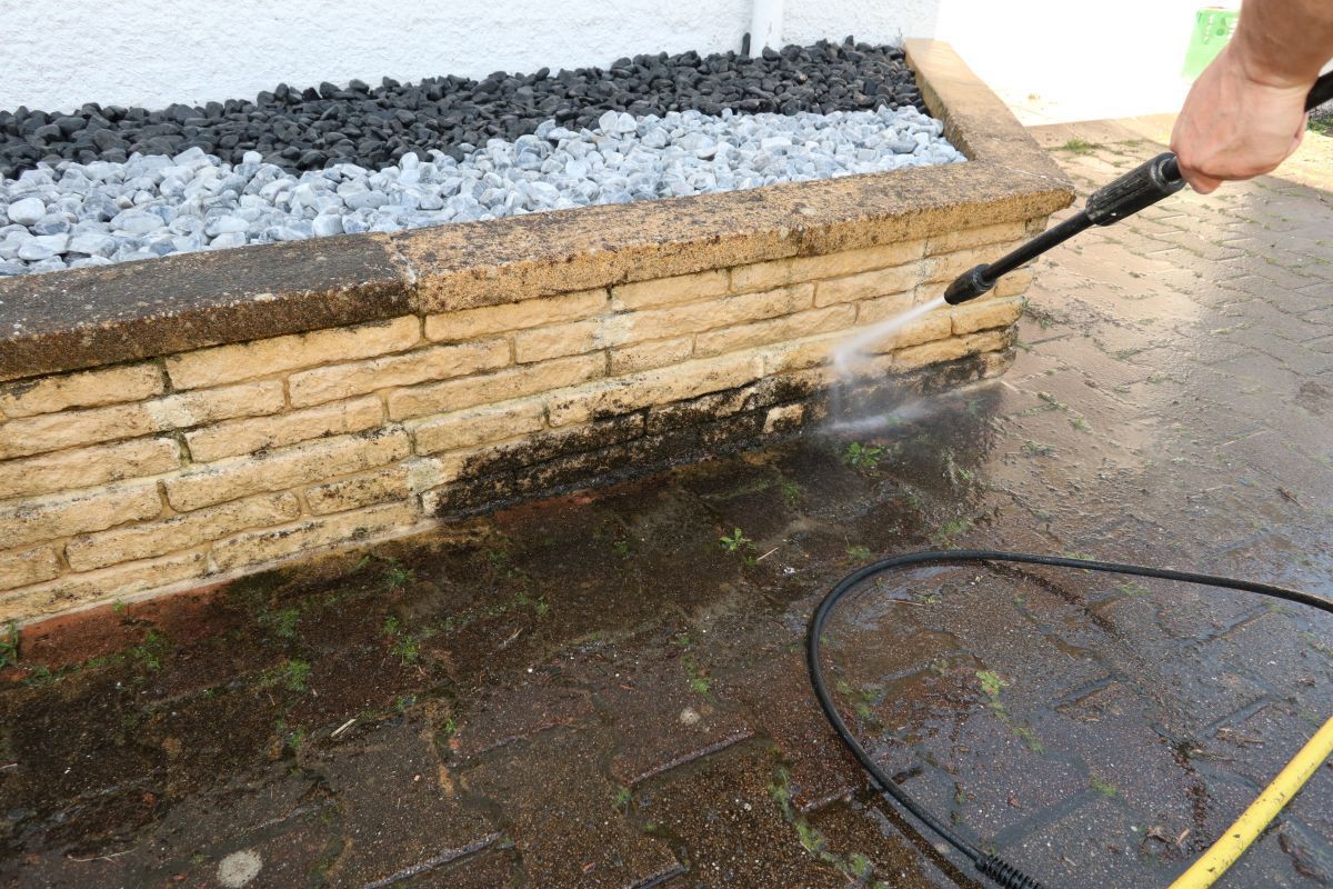 Person pressure-washing a brick planter wall with gray stones on top outdoors in Nashville, TN