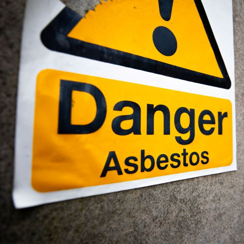 Yellow danger asbestos warning sign on a wall, with a black hazard symbol and bold text in Nashville, TN