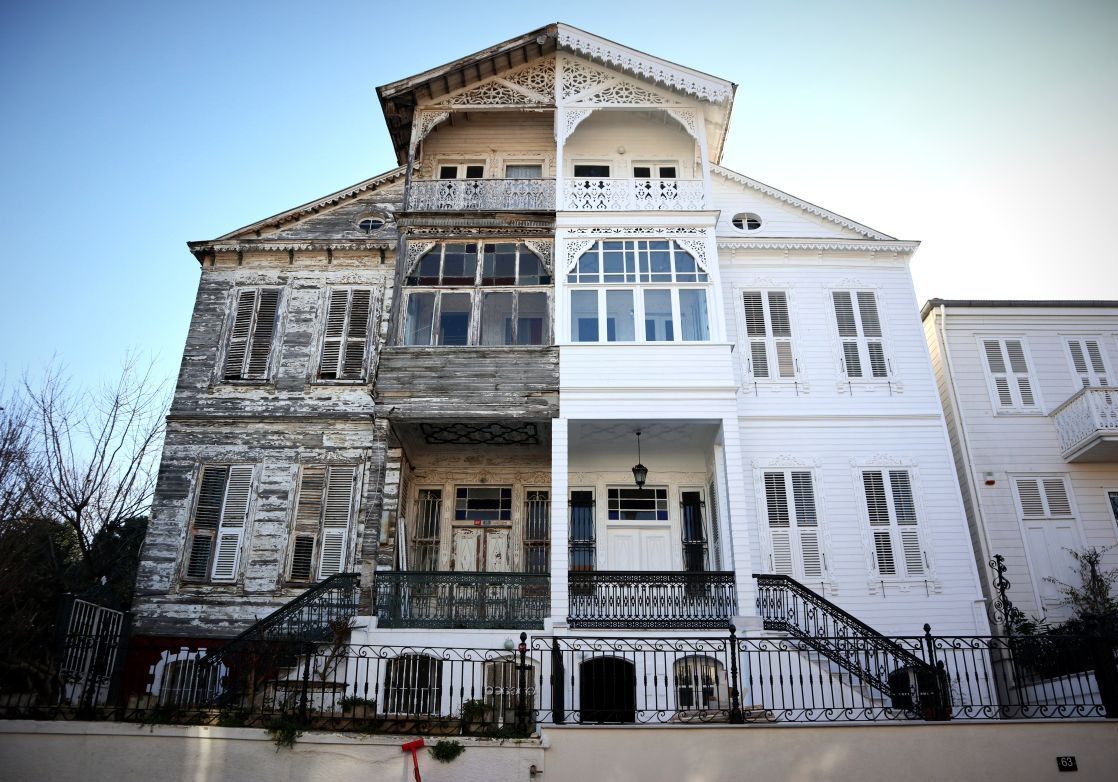 Two-story historic house with weathered gray siding beside a white building, front stairs, and black railing in Nashville, TN
