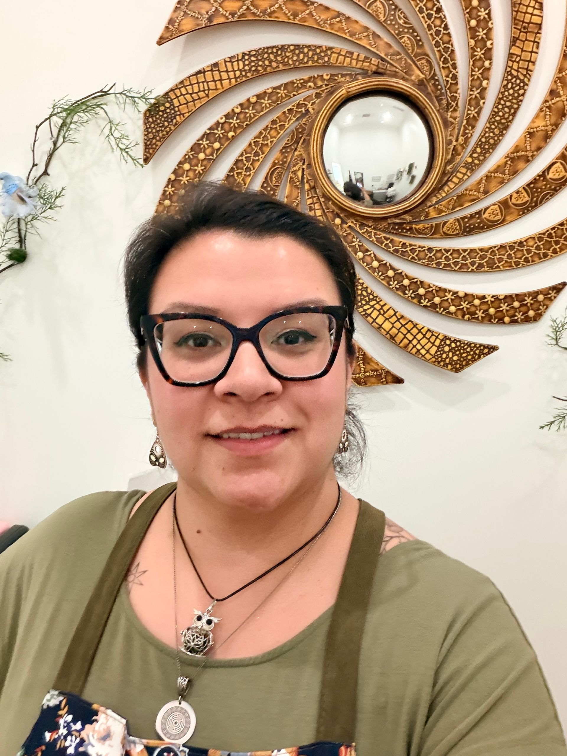 Person with glasses smiling in front of a decorative gold spiral wall mirror