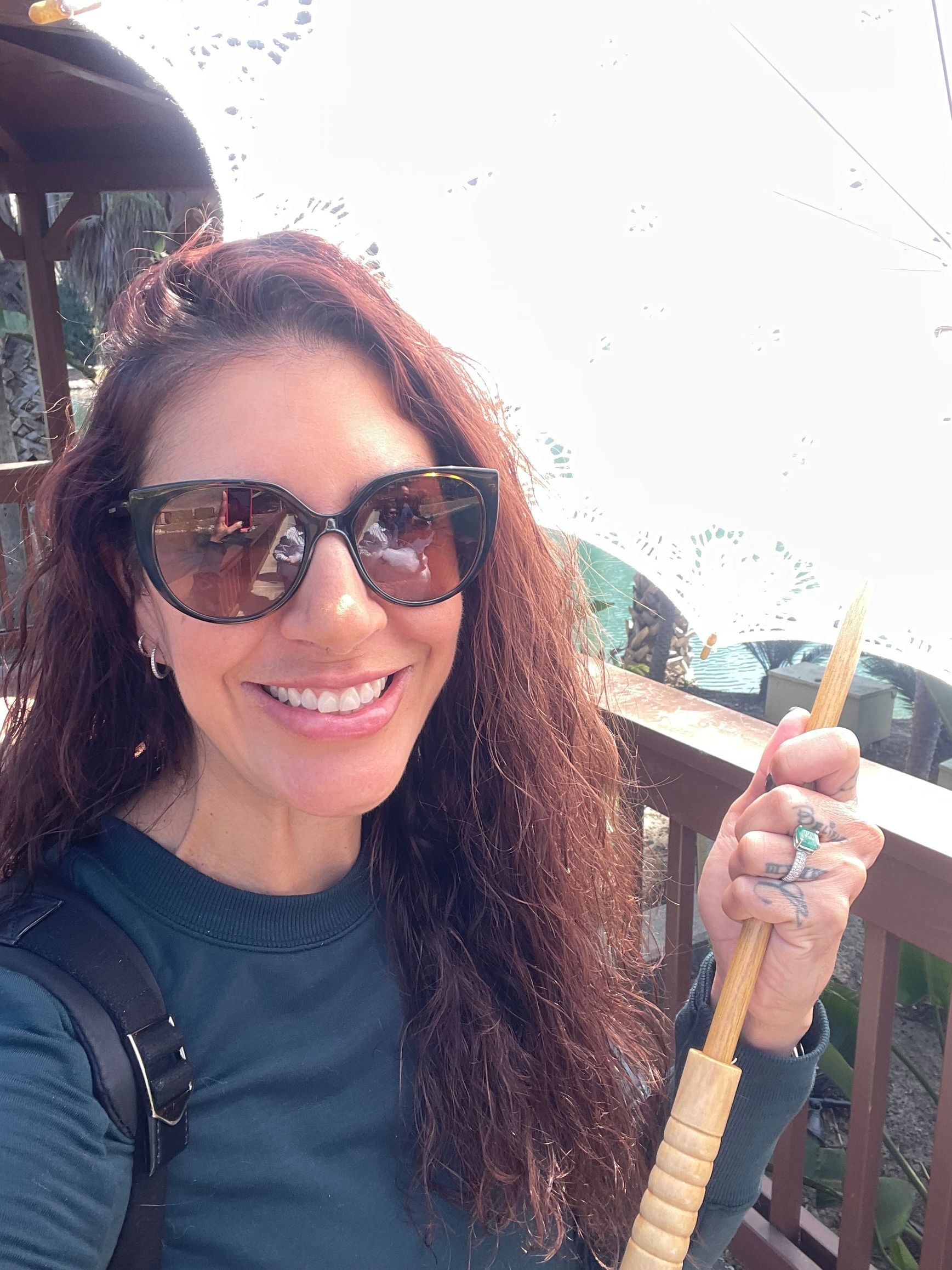 Smiling person in sunglasses holding a broom on a balcony outdoors