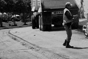 A black and white photo of a man standing in front of a dumpster.