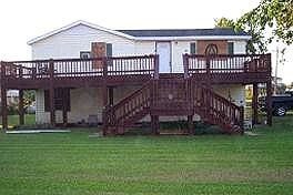 A white house with a large wooden deck and stairs.