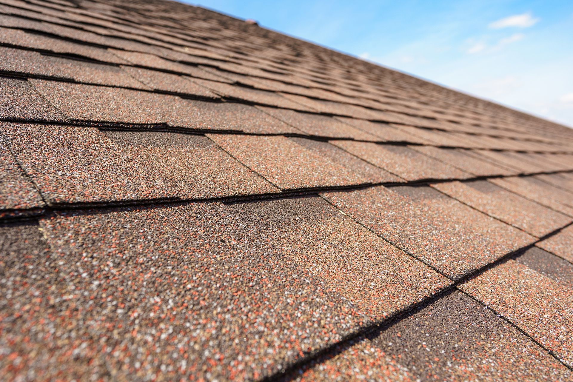 A close up of a roof with shingles against a blue sky.