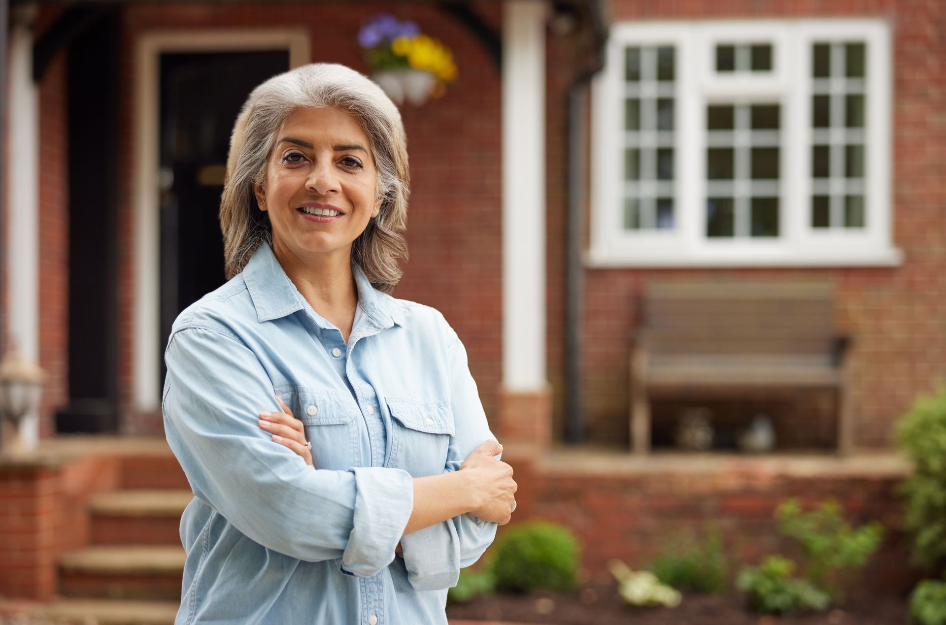 A woman is standing in front of a brick house with her arms crossed.