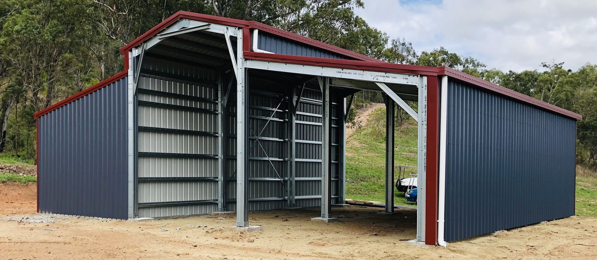 A Partially Enclosed Blue and Red Metal Barn Structure with An Open Front Bay — BF Sheds & Garages In Rockhampton, QLD