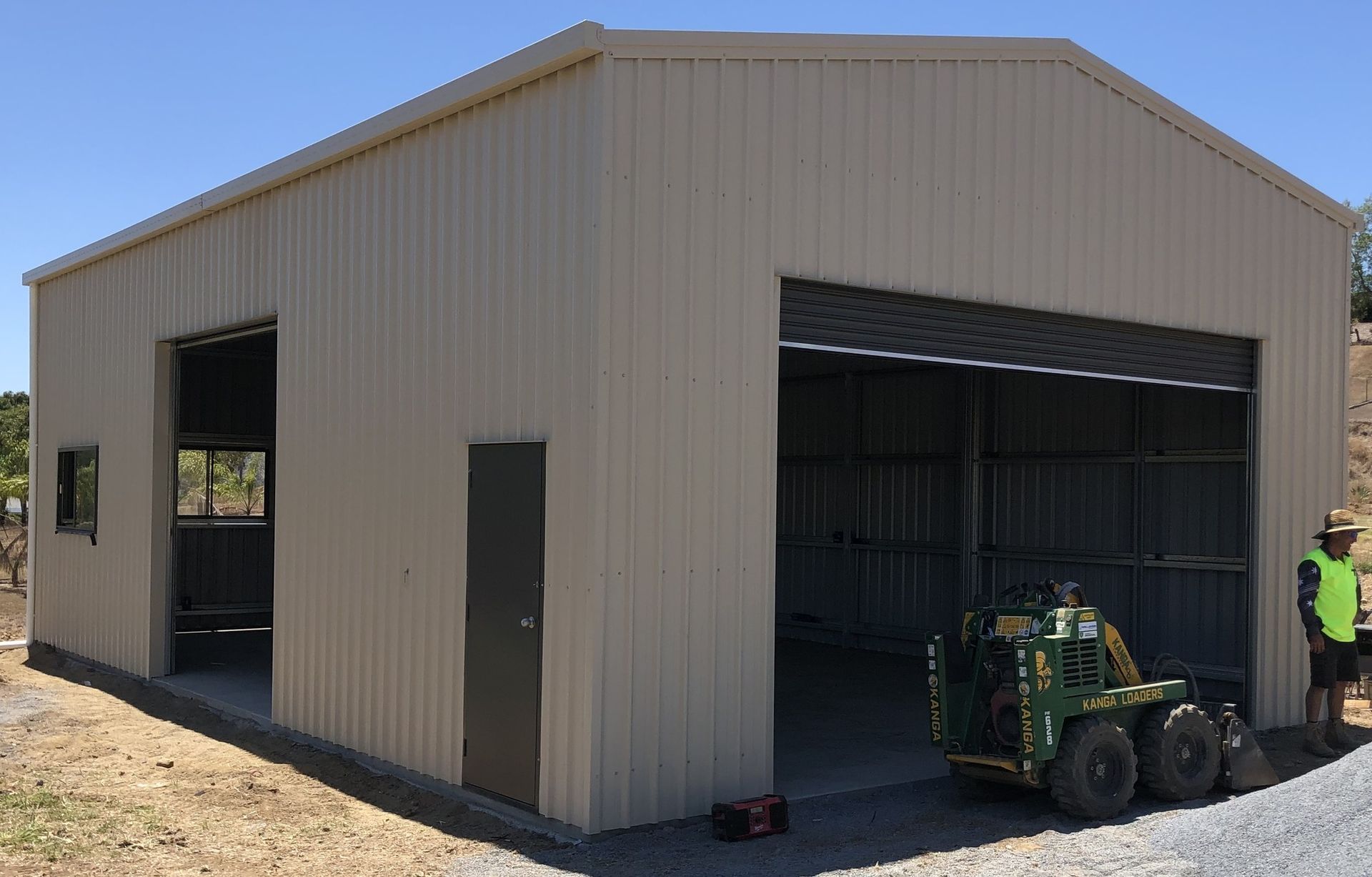 Beige Metal Shed Under Construction with A Large Open Roller Door — BF Sheds & Garages In Rockhampton, QLD