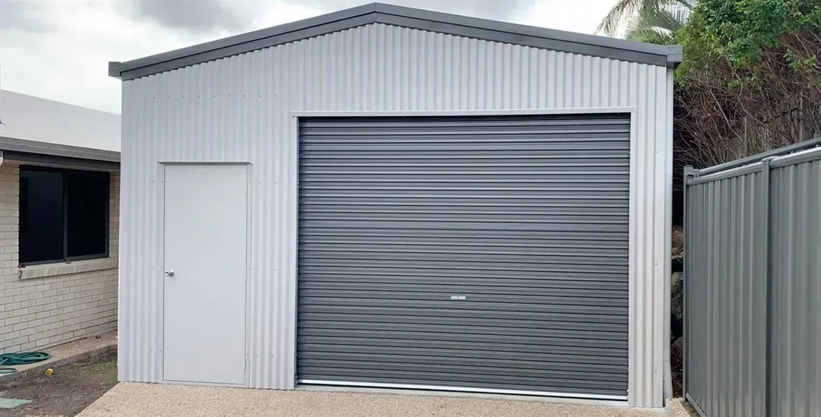 A Corrugated Metal Shed with A Gray Roller Door and A Small White Side Entrance Door — BF Sheds & Garages In Rockhampton, QLD