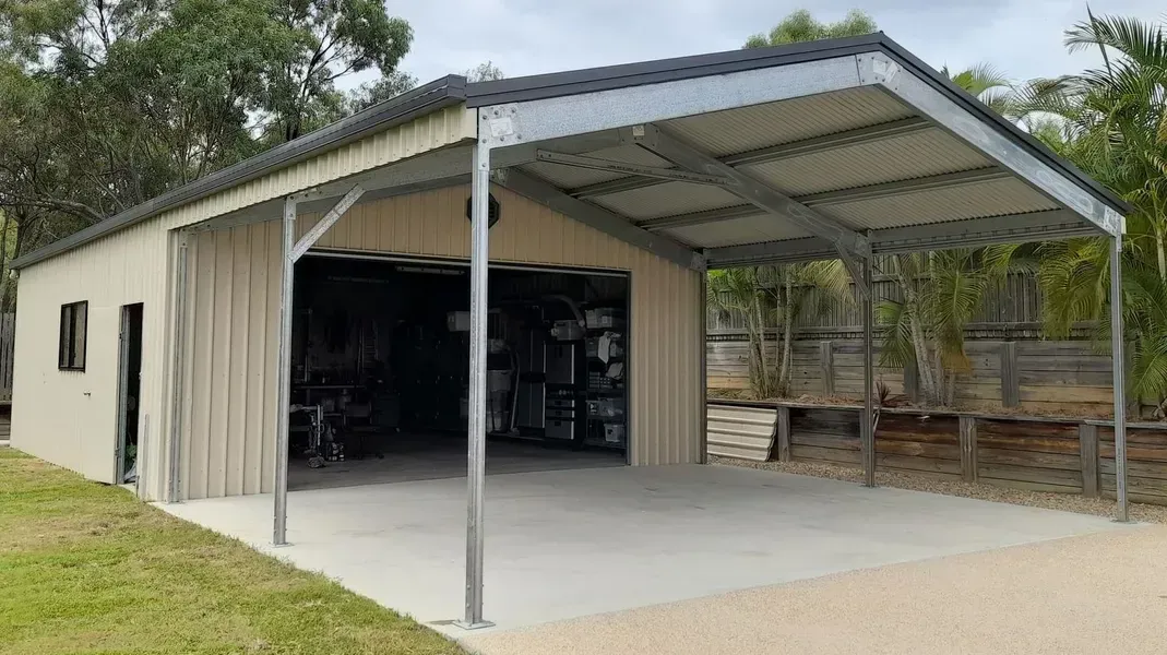 A Beige Metal Shed with An Open, Covered Carport Area, Set on A Concrete Slab in A Grassy Yard — BF Sheds & Garages In Rockhampton, QLD