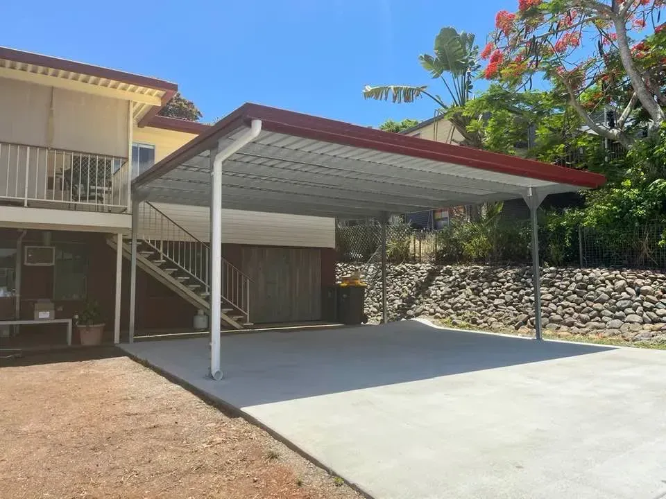 A Modern White House with A Covered Carport Over a Concrete Driveway, Next to A Rock Retaining Wall and Green Trees — BF Sheds & Garages In Rockhampton, QLD