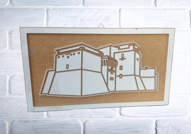 Disegno stilizzato di edifici su sfondo beige, incorniciato e appeso a un muro di mattoni bianchi.