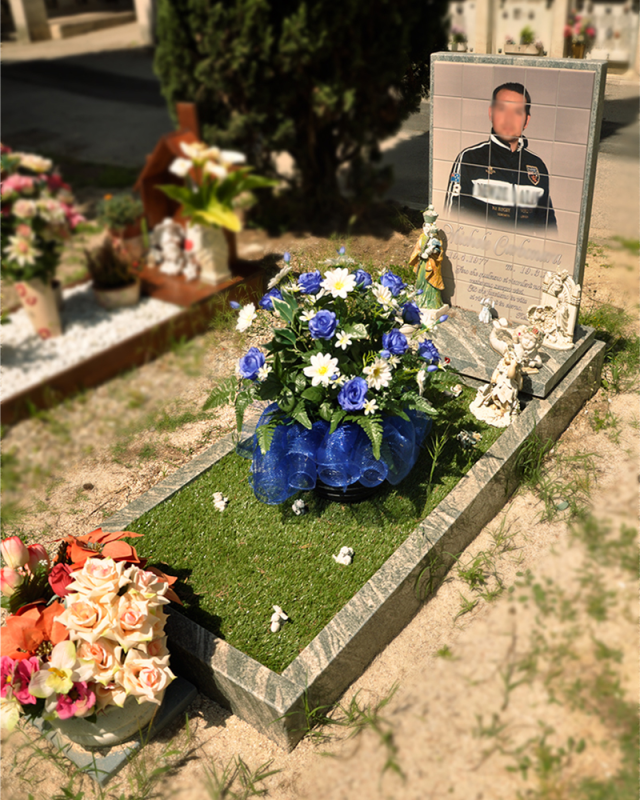 Lapide con ritratto, fiori bianchi e blu e mazzi di fiori in un cimitero
