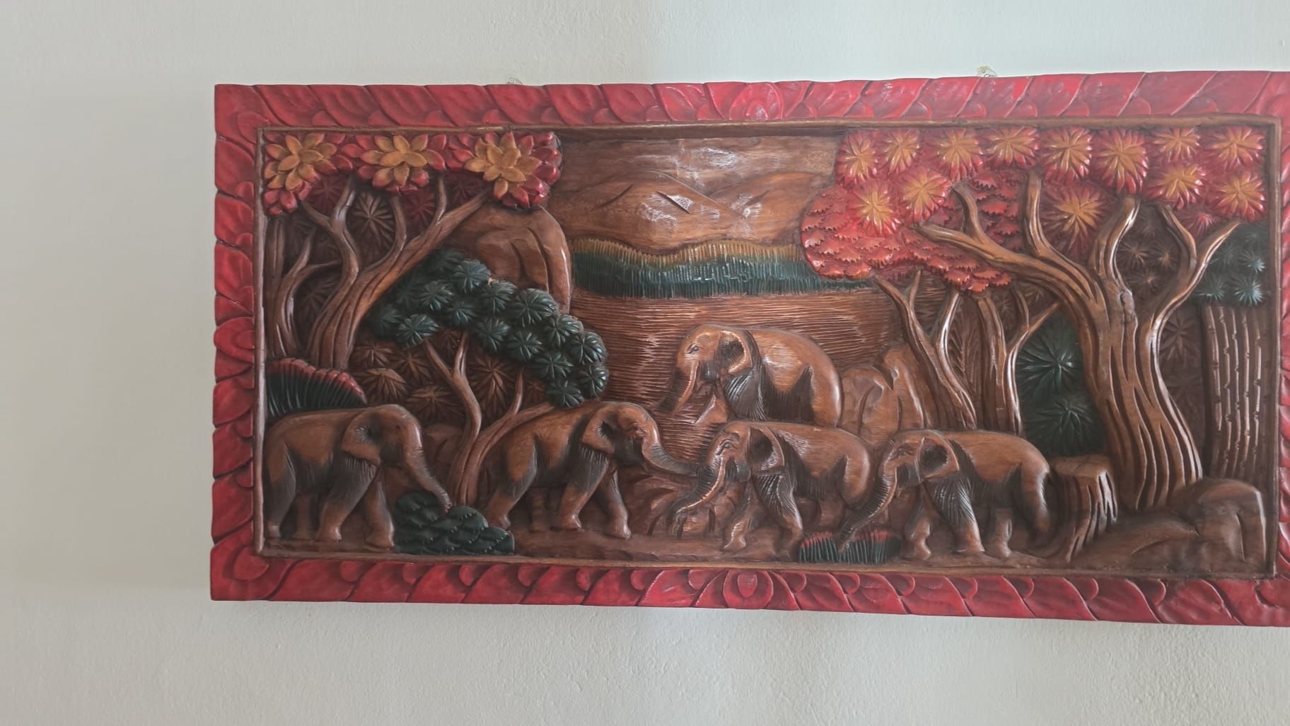 Una targa murale scolpita con bordo rosso raffigura degli elefanti che camminano in una foresta.