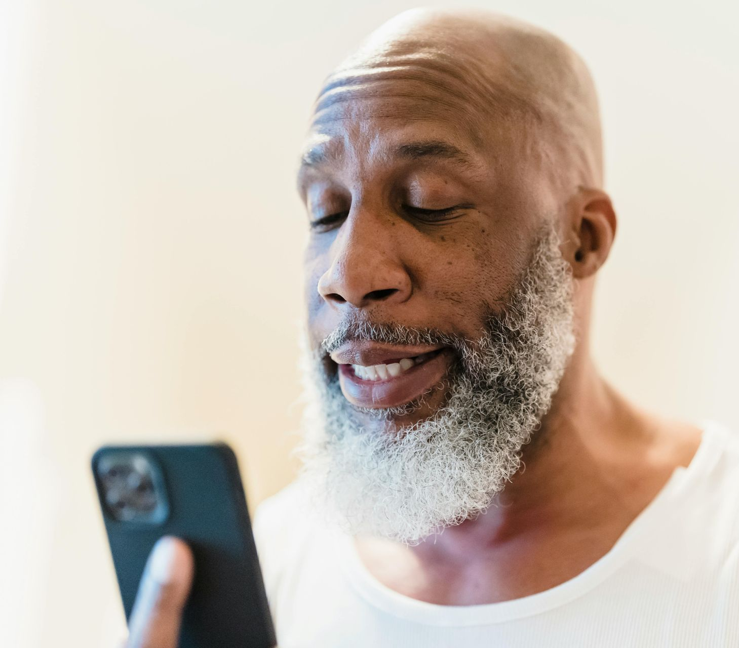 Man with a gray beard looking at a smartphone, smiling.