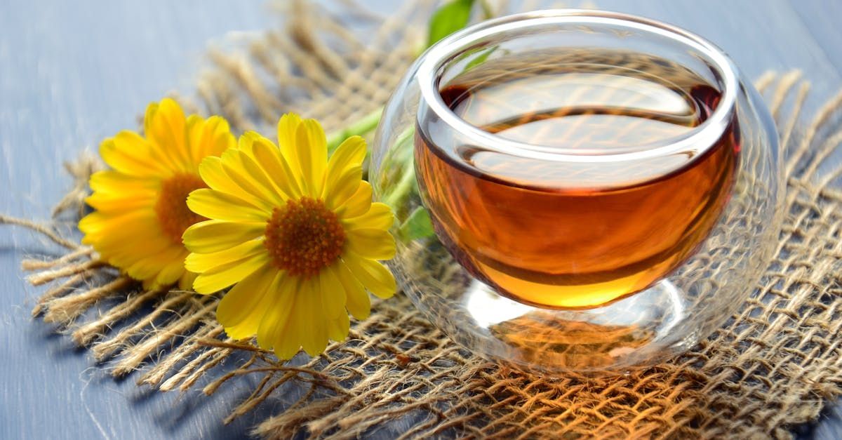 A cup of tea is sitting on a table next to a yellow flower.
