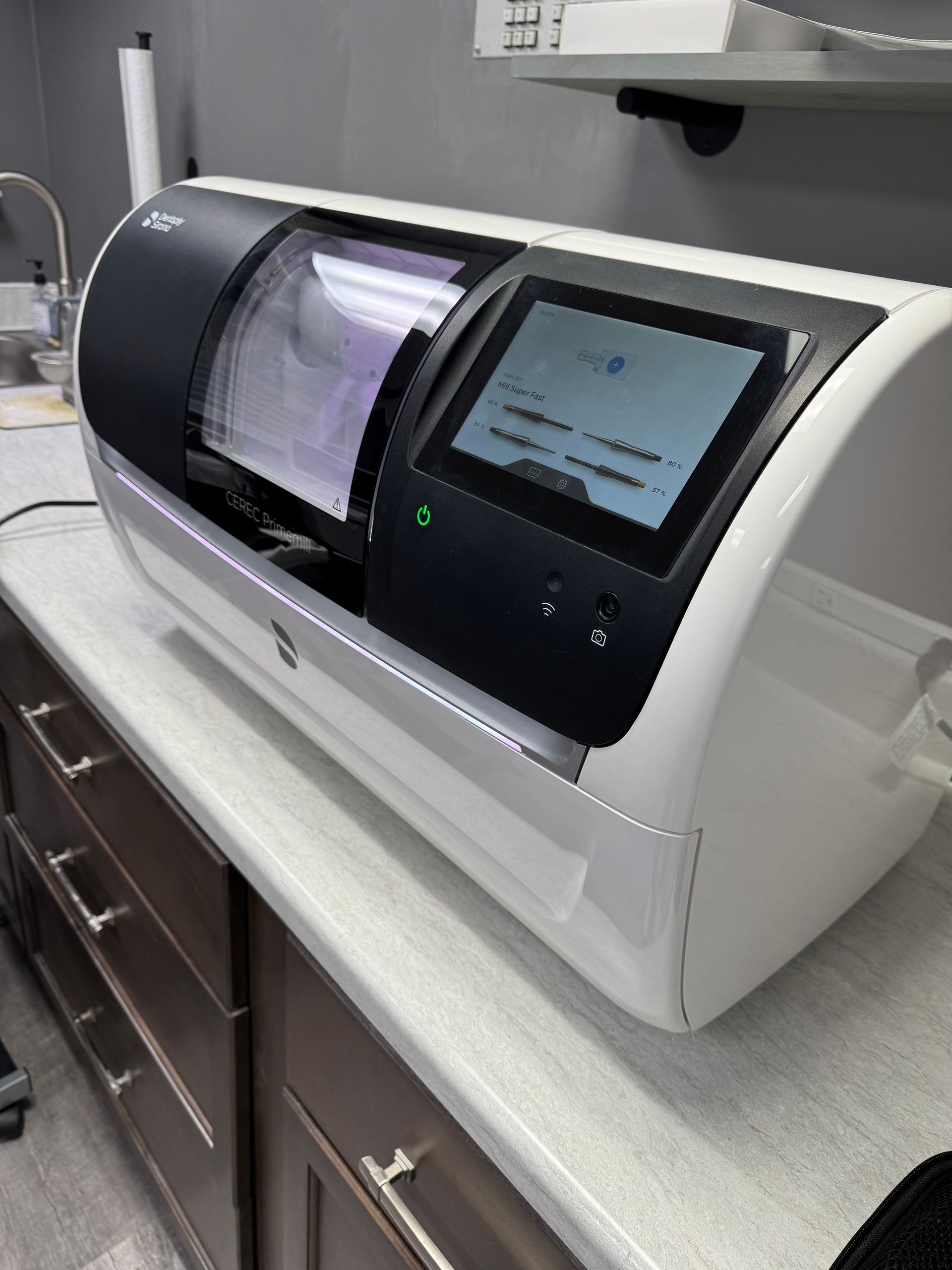 White and black dental milling machine on a countertop with a screen displaying text.