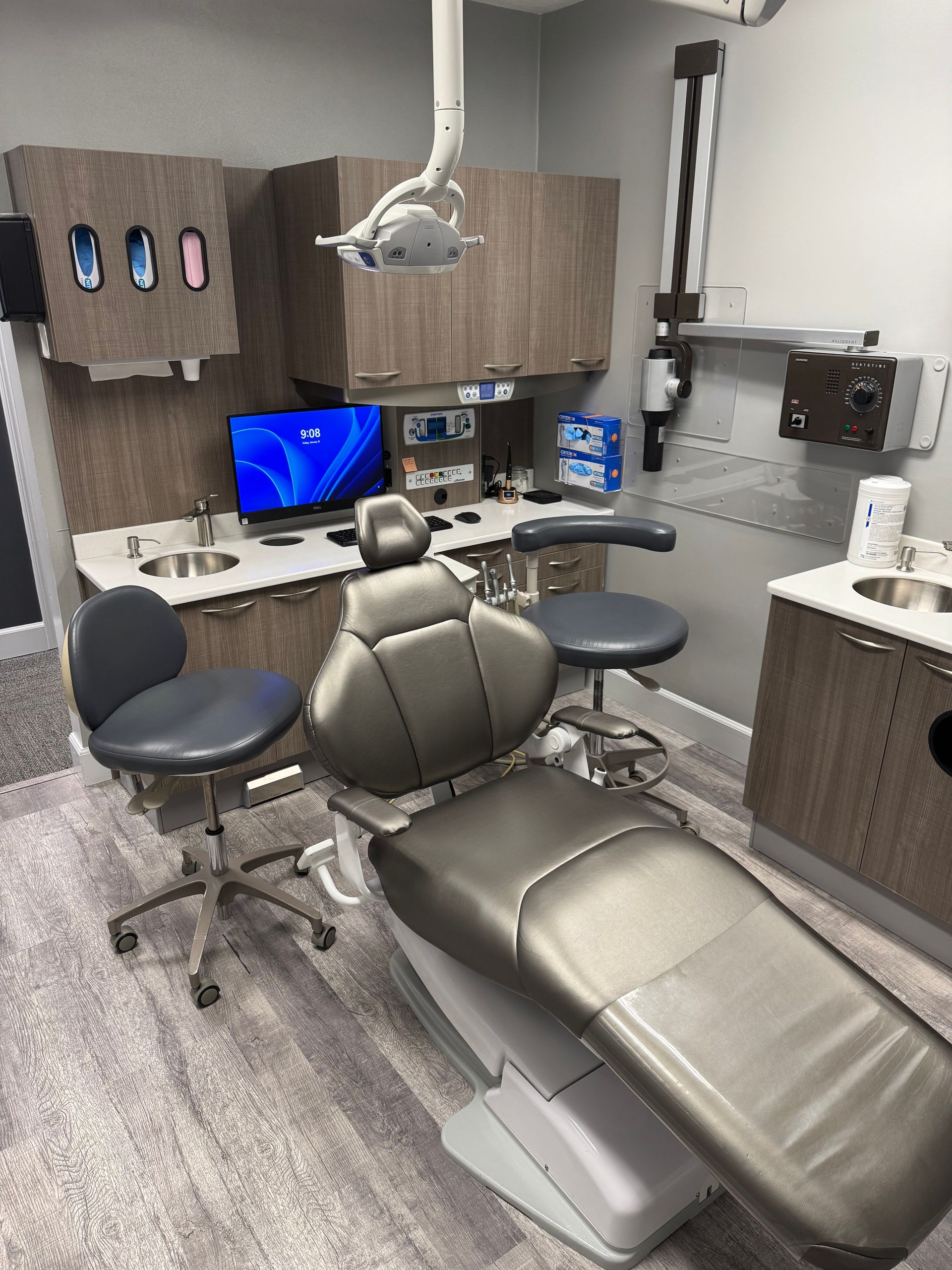 Dental examination room with chair, cabinets, tools, and a computer.