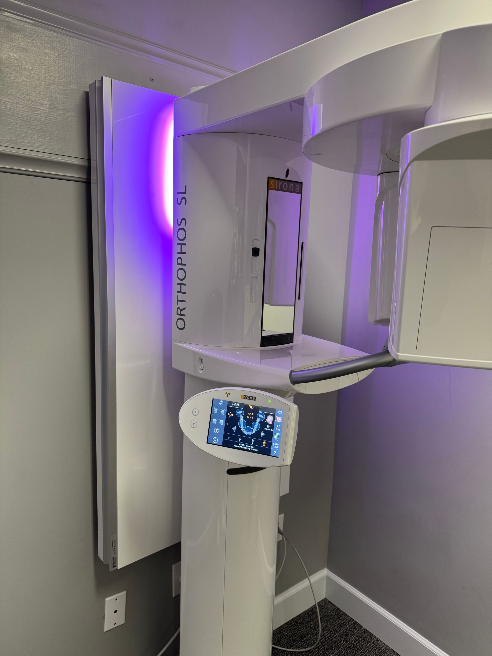 Dental x-ray machine, Orthophos SL, in a dental office. White and silver with a purple light.