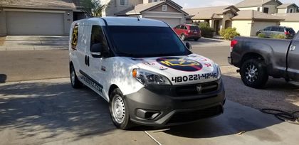 White service van parked on a residential street, with a colorful logo on the hood and black rear panels.