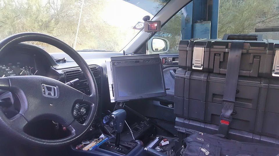 Interior of a vehicle cab with steering wheel, mounted screen, and storage boxes beside the passenger seat.