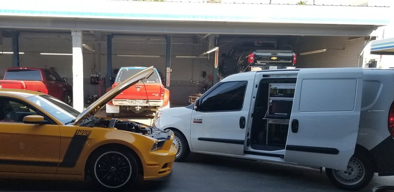 Yellow sports car and white van parked in front of a garage, with the van’s sliding door open.