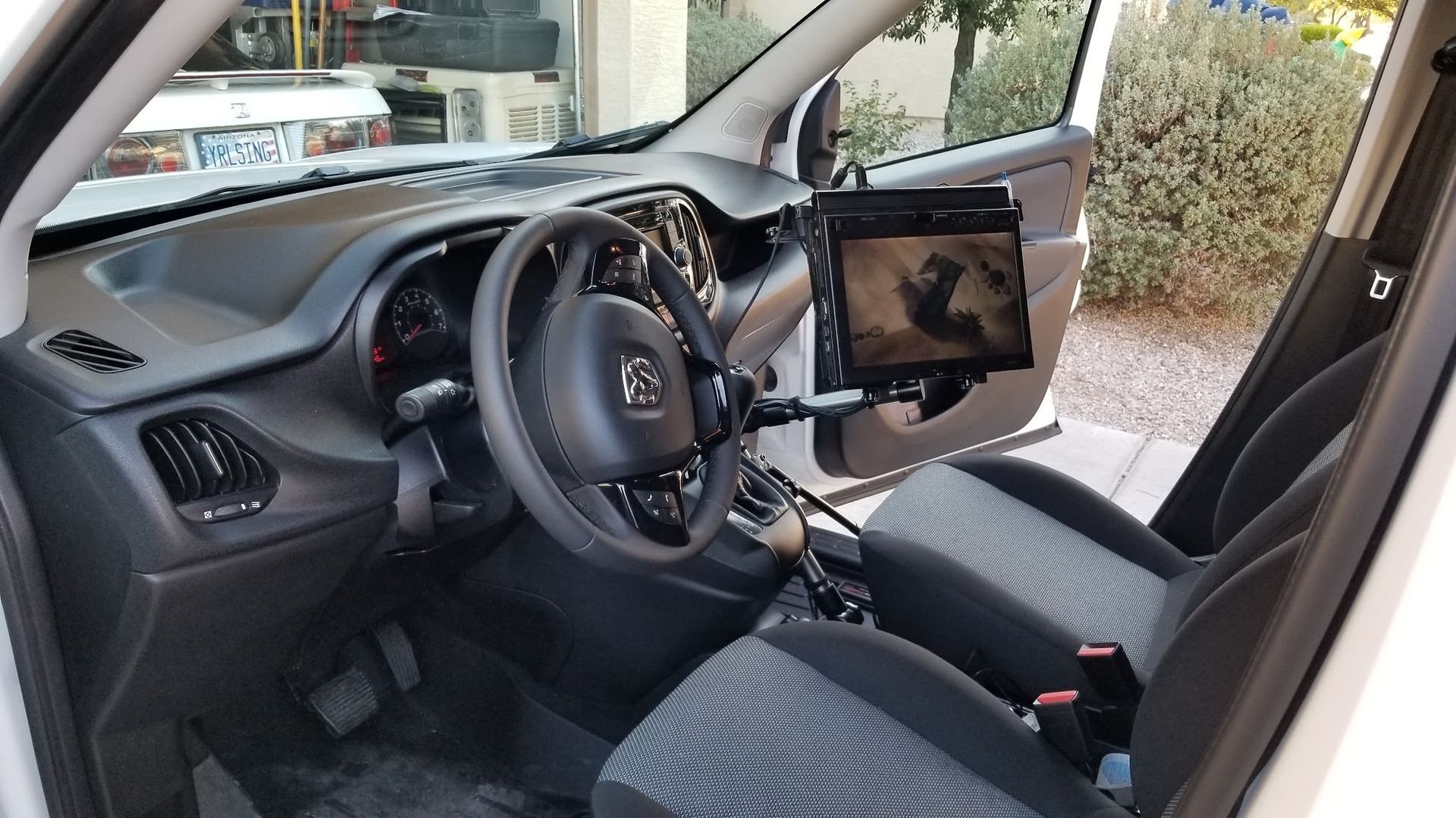 Car interior with open driver door, steering wheel, dashboard, and a tablet mounted near the center console.