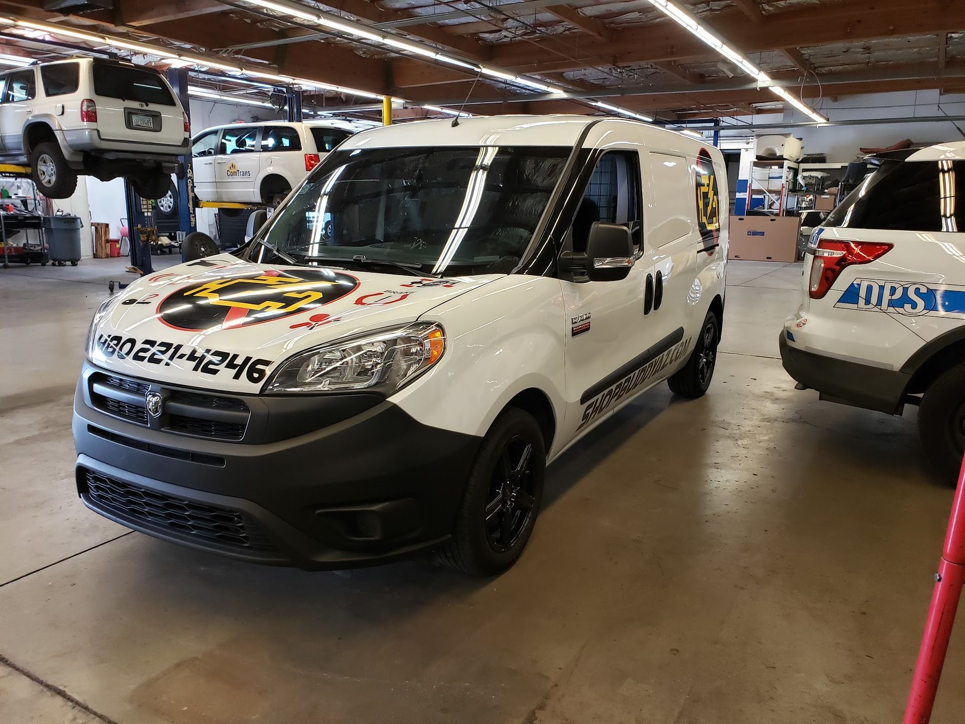 White van with racing-style decals in an indoor garage, parked among other vehicles.