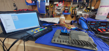 Workbench with laptop, keyboard, tools, and circuit boards in a cluttered electronics repair area