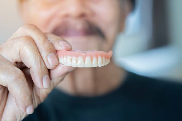 An old happy man in black t-shirt showing a model of human teeth.