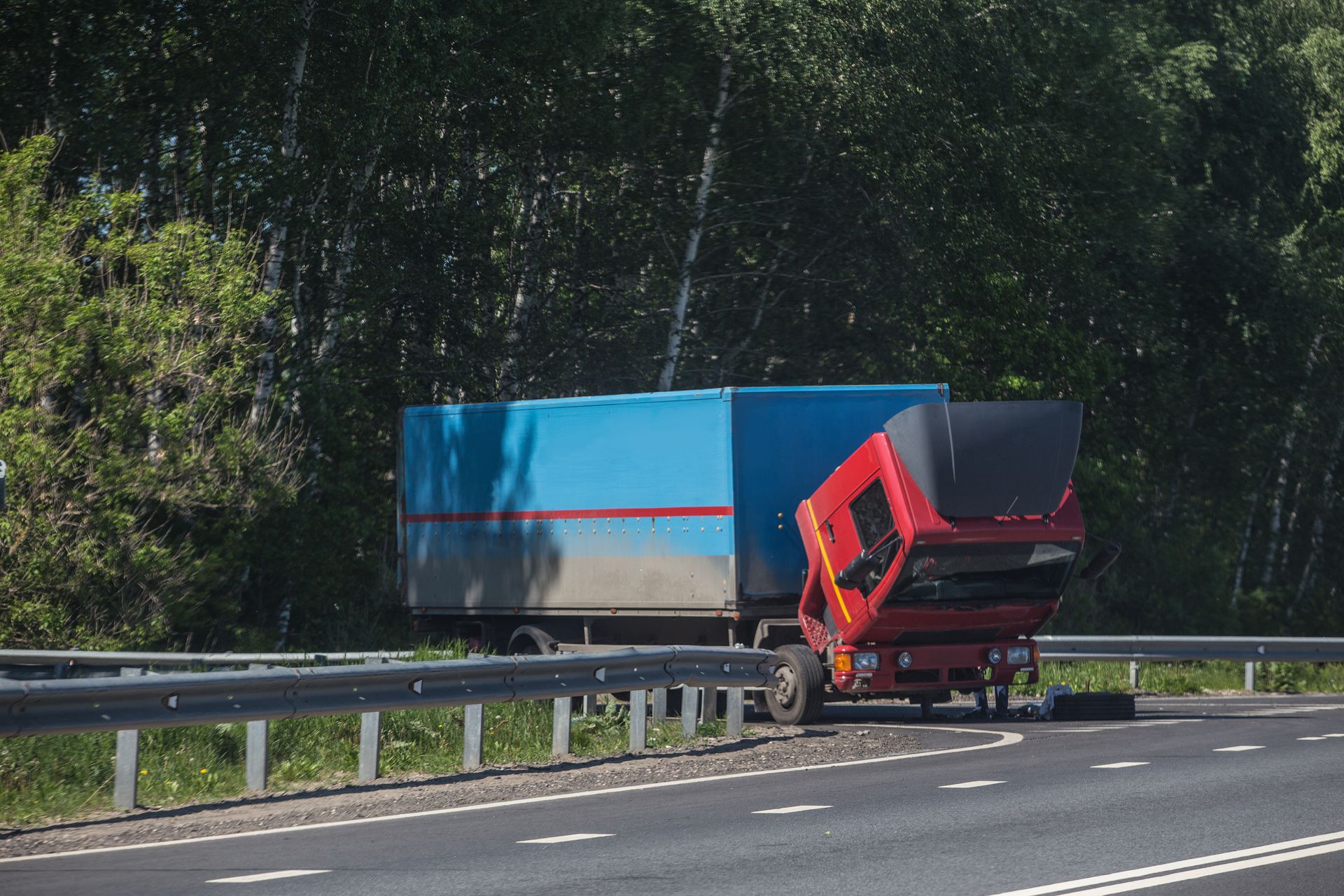 A red truck has crashed into a blue truck on the side of a highway.