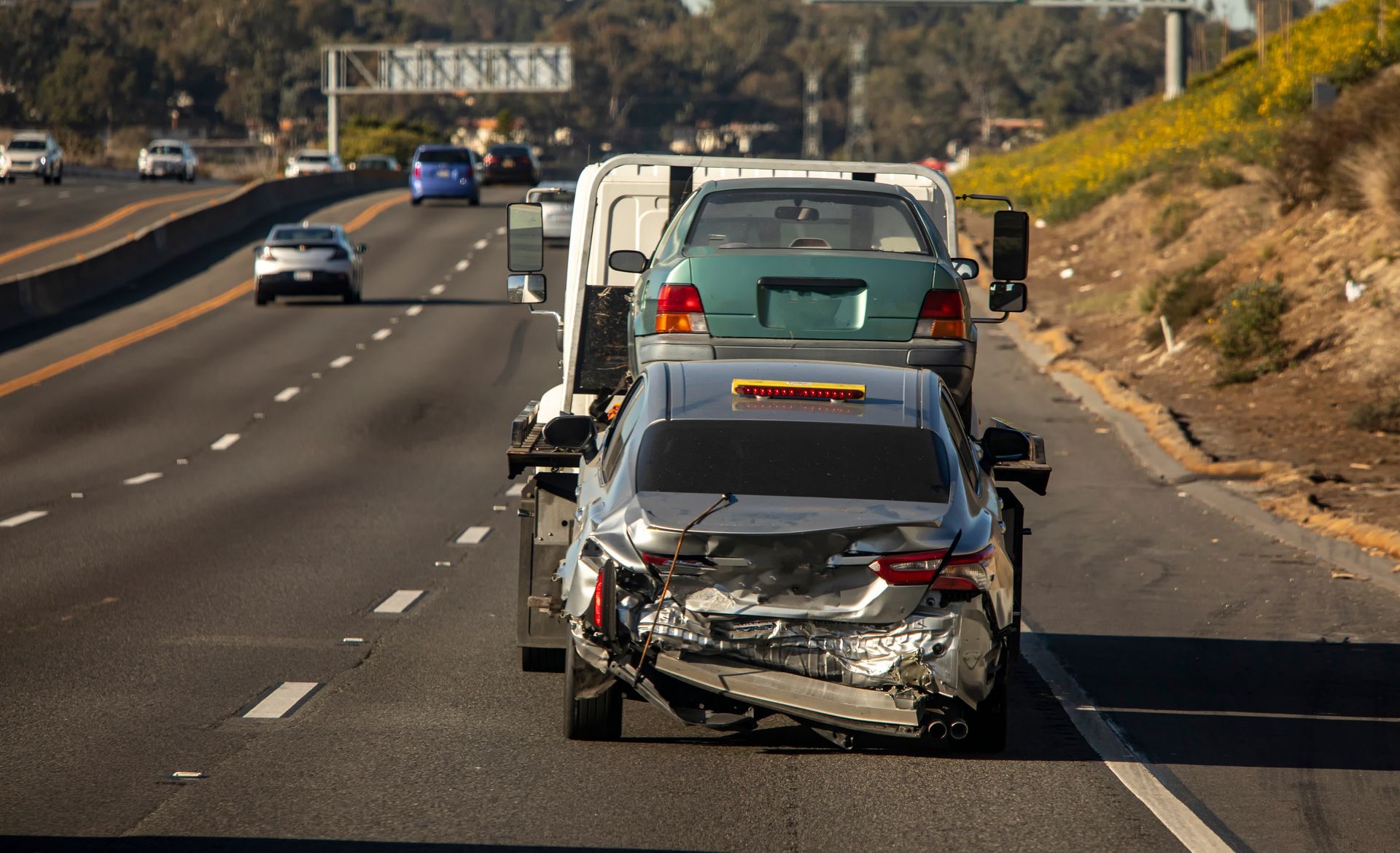 A car is being towed down a highway by a tow truck.