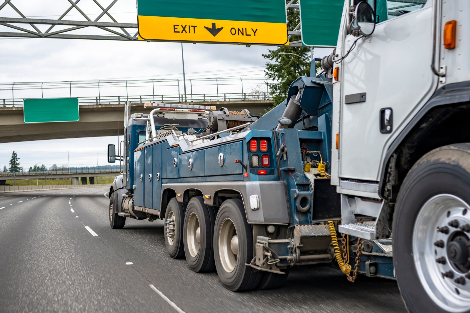 A tow truck is driving down a highway under a sign that says exit only.