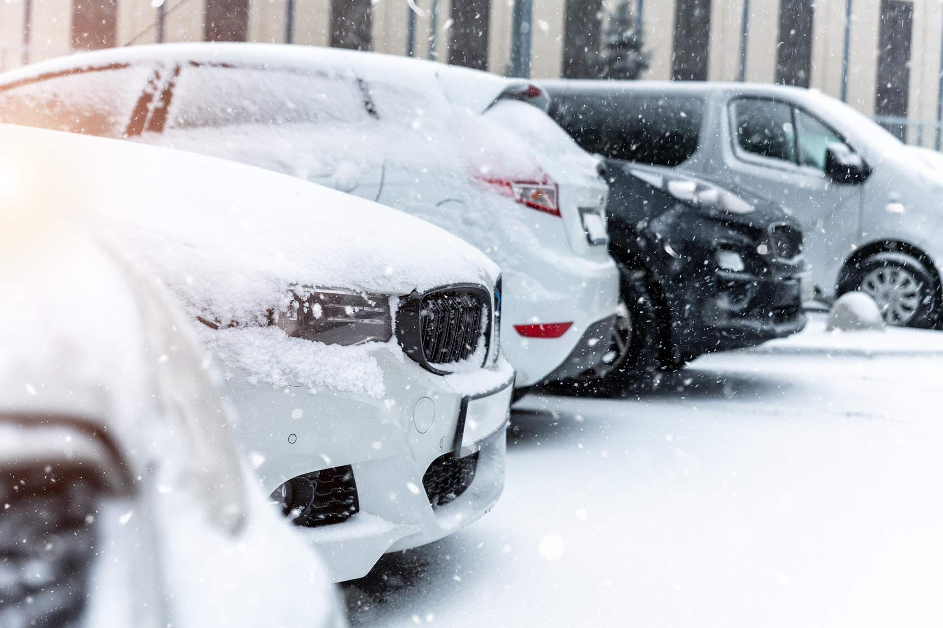 A row of cars covered in snow in a parking lot.
