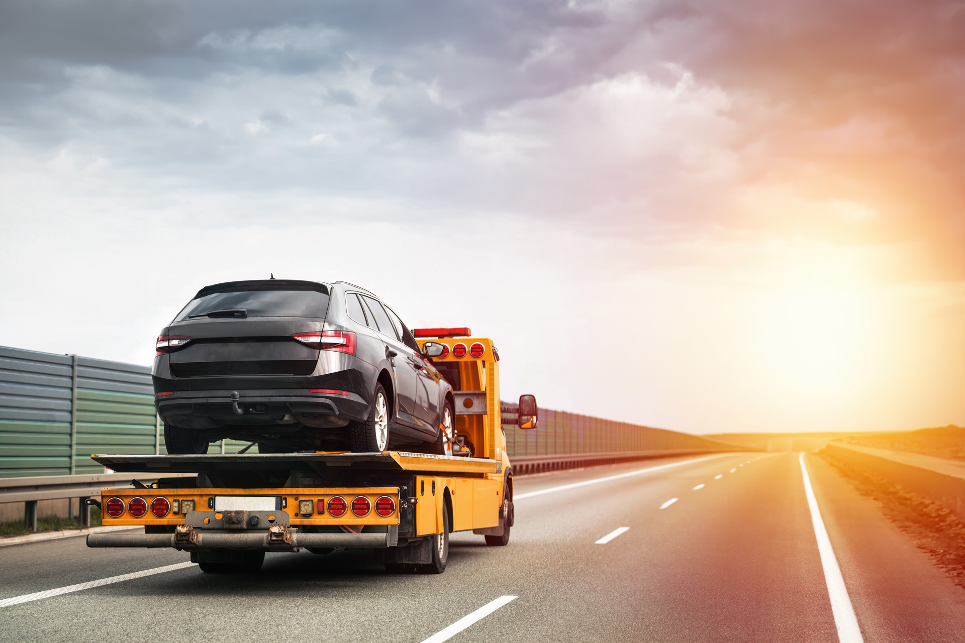A tow truck is towing a car on the highway.