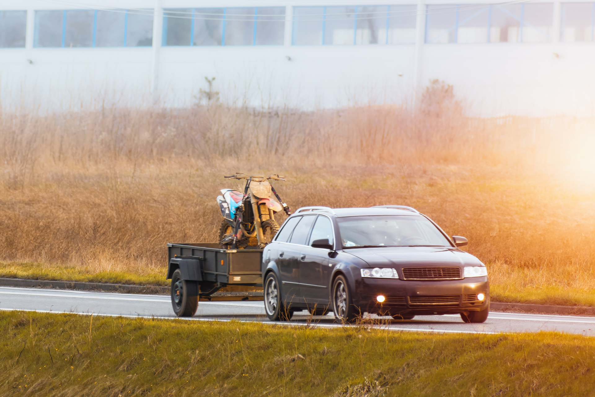 A car is towing a trailer with a motorcycle on it.