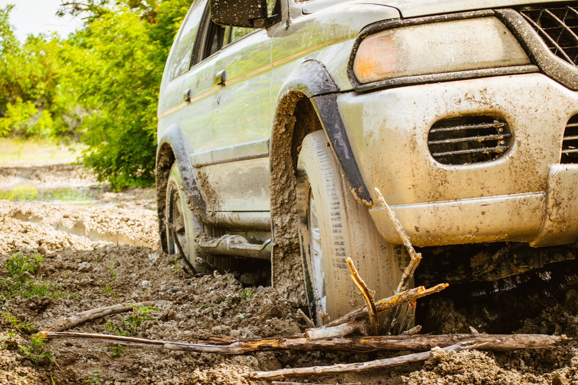 A muddy suv is stuck in the mud on a dirt road.