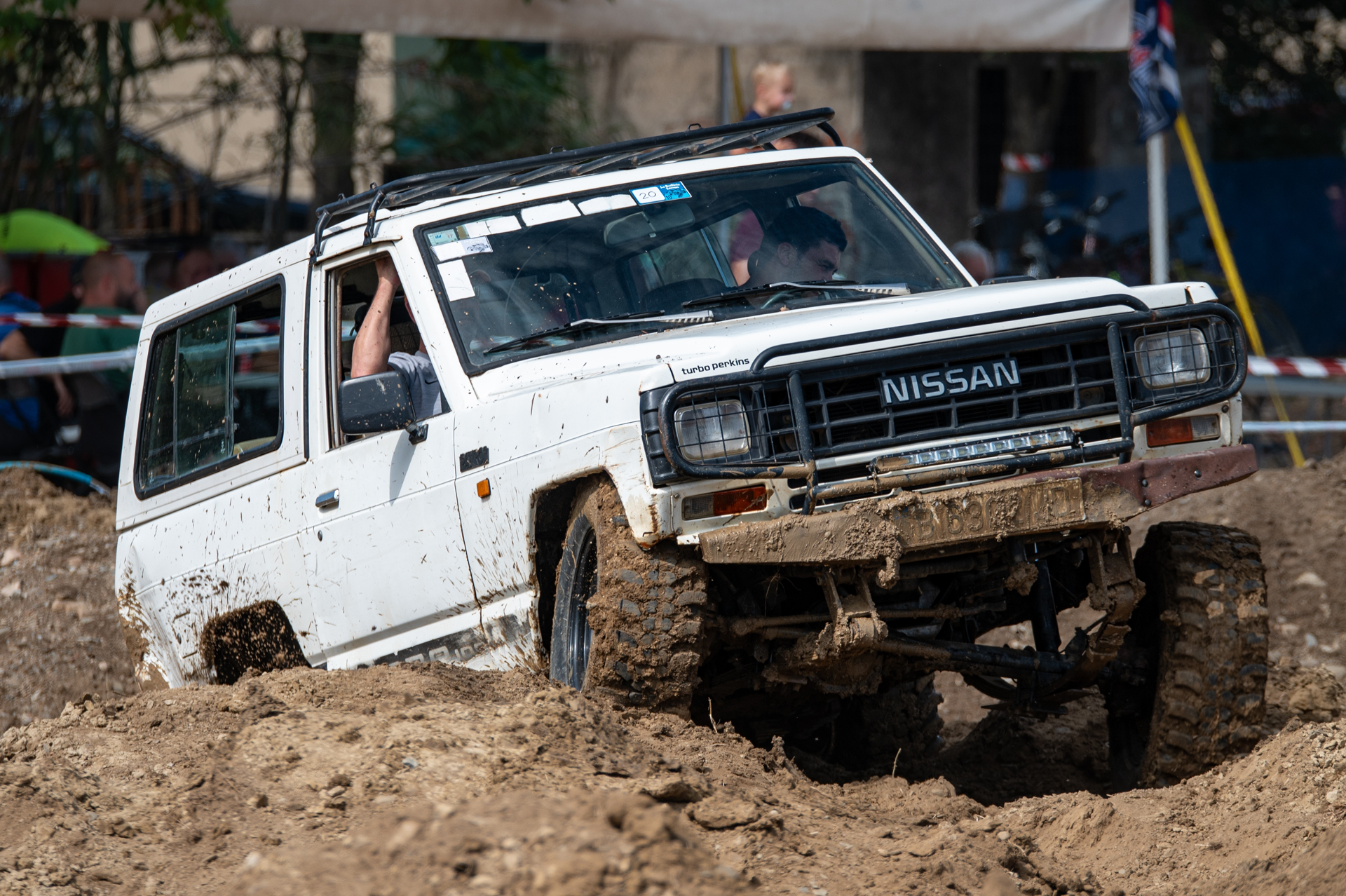 A white nissan truck is driving through the mud.