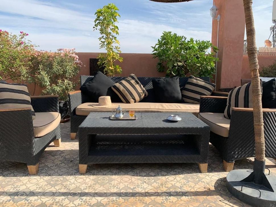 Outdoor lounge area with black wicker furniture and decorative pillows on a sunny rooftop.