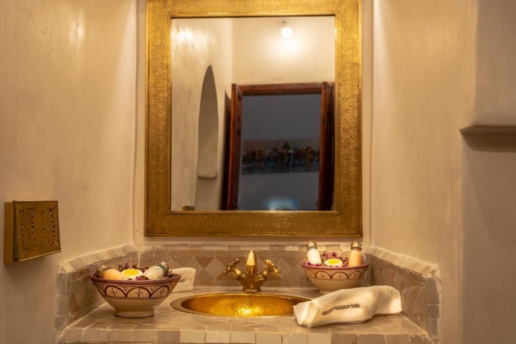 Golden framed mirror above a sink with ornate faucet and two bowls, in a tiled alcove.