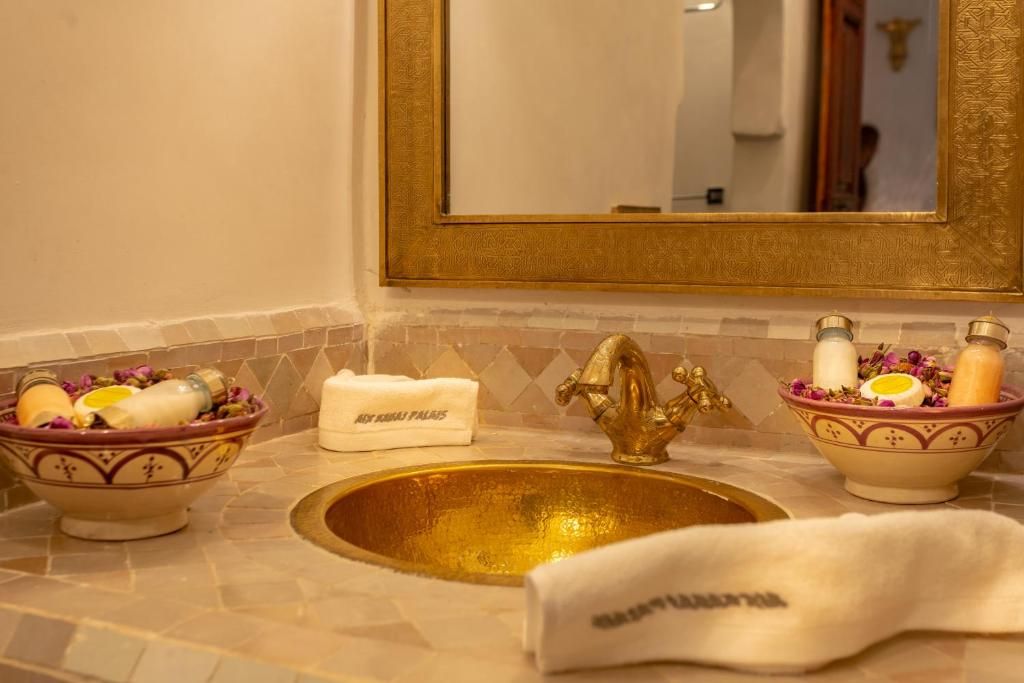 Gold sink basin with ornate faucet, surrounded by decorative bowls of toiletries. Mirror above.