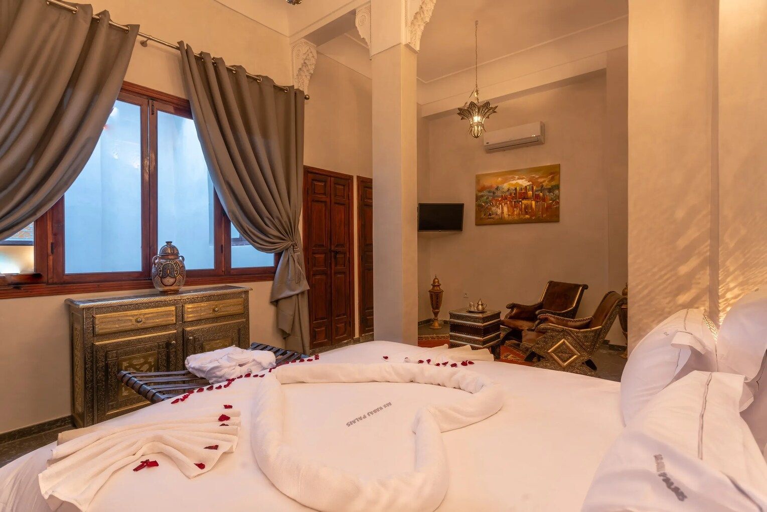 Bedroom with ornate decor, bed with towel art, window, seating area, artwork.