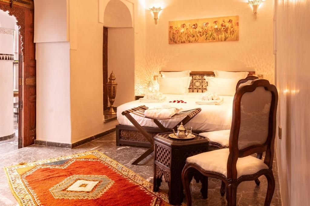 Cozy bedroom with ornate rug, carved wood furniture, and bed with pillows and tray of tea.