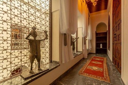 Hallway with patterned window, sculpture, red rug, white curtains, and wooden doors.